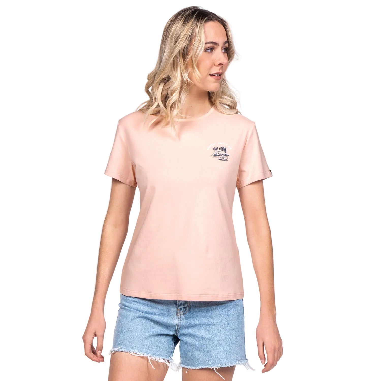 A woman modeling a pink crew neck t-shirt with a small graphic print in the center, paired with denim shorts.