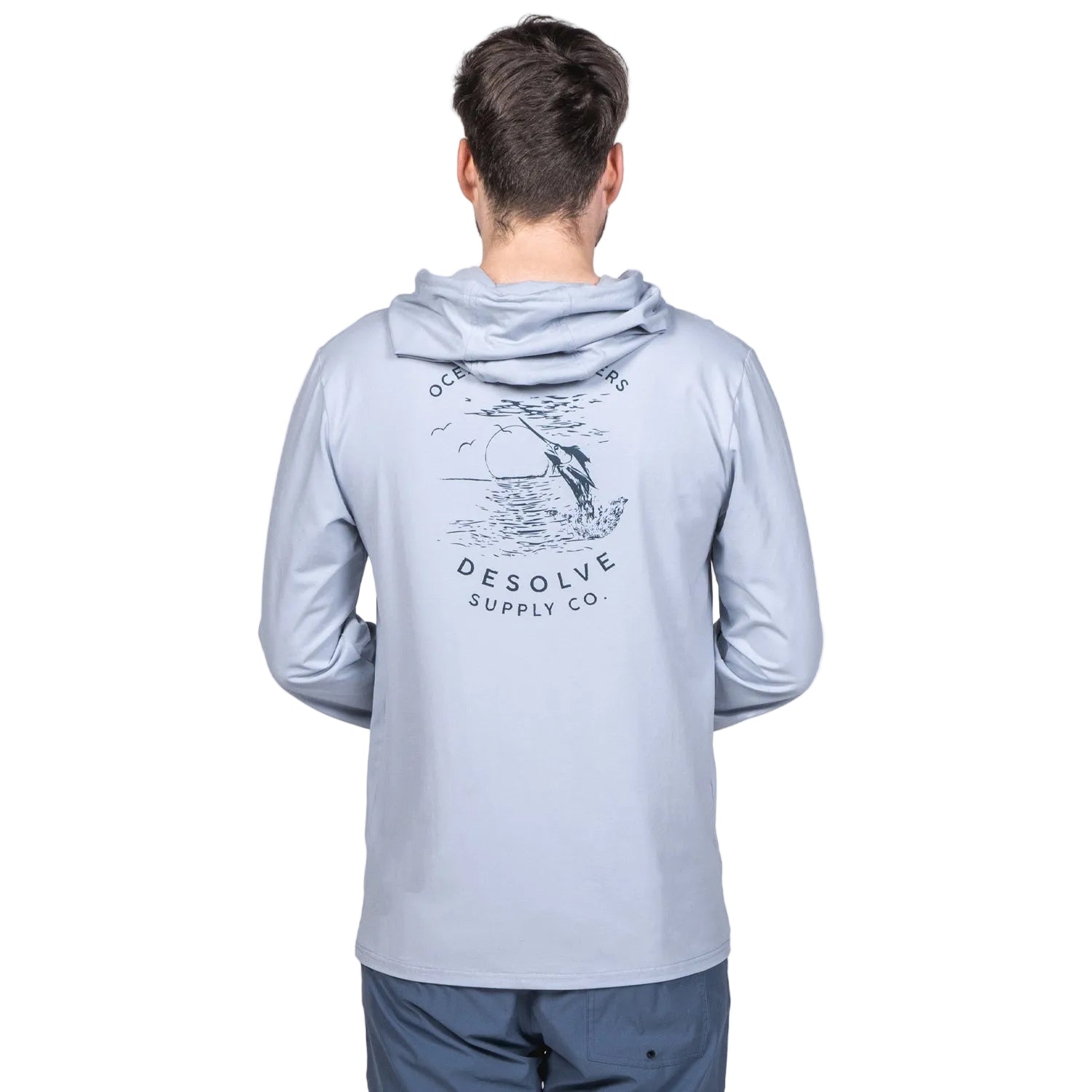 A person wearing a light blue hoodie with a graphic print on the back, featuring a bird and the text 'desolate supply co.' The hoodie has a hood and is styled in a casual, loose fit.