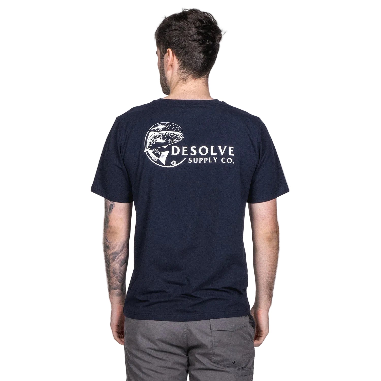 A person viewed from behind wearing a beige t-shirt with 'DESOLVE SUPPLY CO' and a graphic of a fish printed on the back.